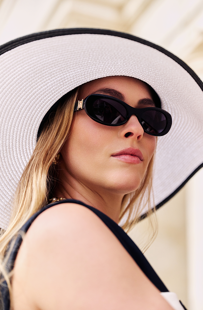 Woman wearing white wide-brimmed hat and dark sunglasses, looking over shoulder