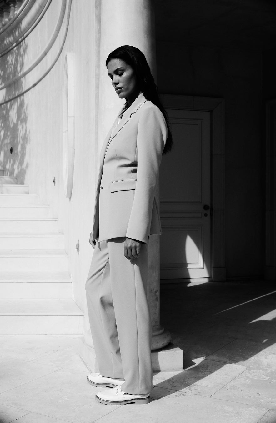 Anne Klein cream blazer and wide-leg trousers on model with white sneakers, architectural setting
