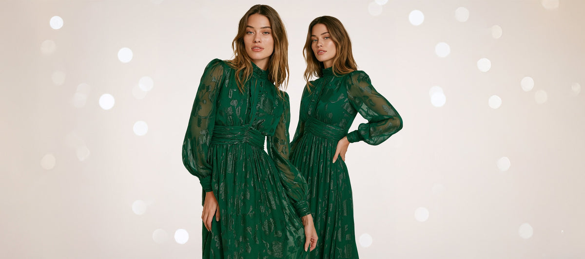 Two women in elegant green dresses posing against a bokeh light background