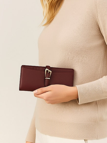 Woman holding a burgundy wallet with a silver buckle against a beige sweater