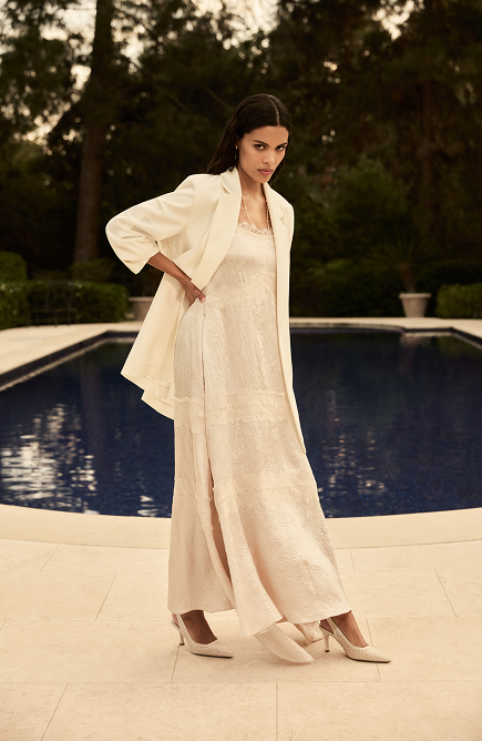 Woman in cream linen dress and blazer standing by pool