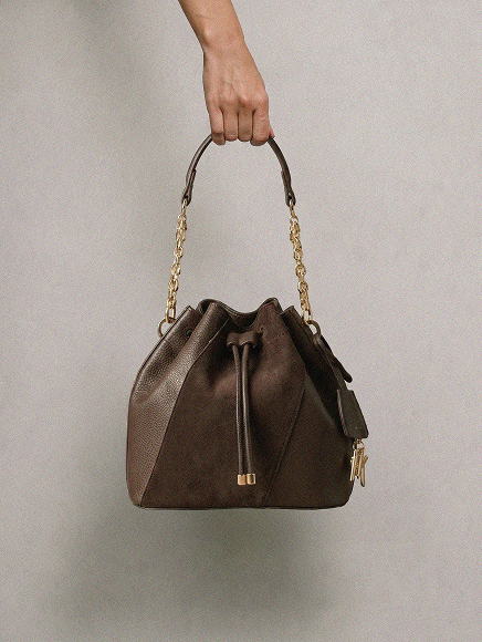 Brown leather bucket handbag with chain strap held by hand against neutral background