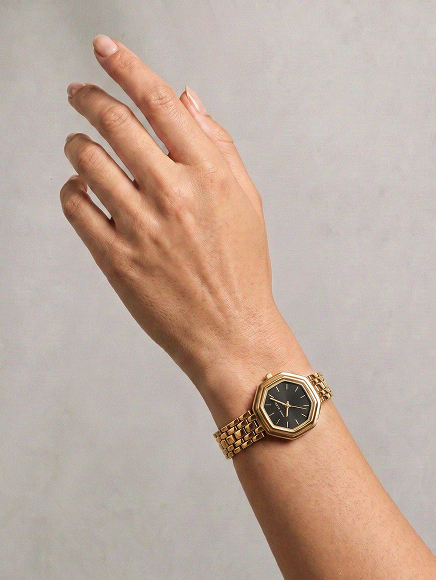 Woman's wrist wearing gold-tone watch with black dial and mesh bracelet