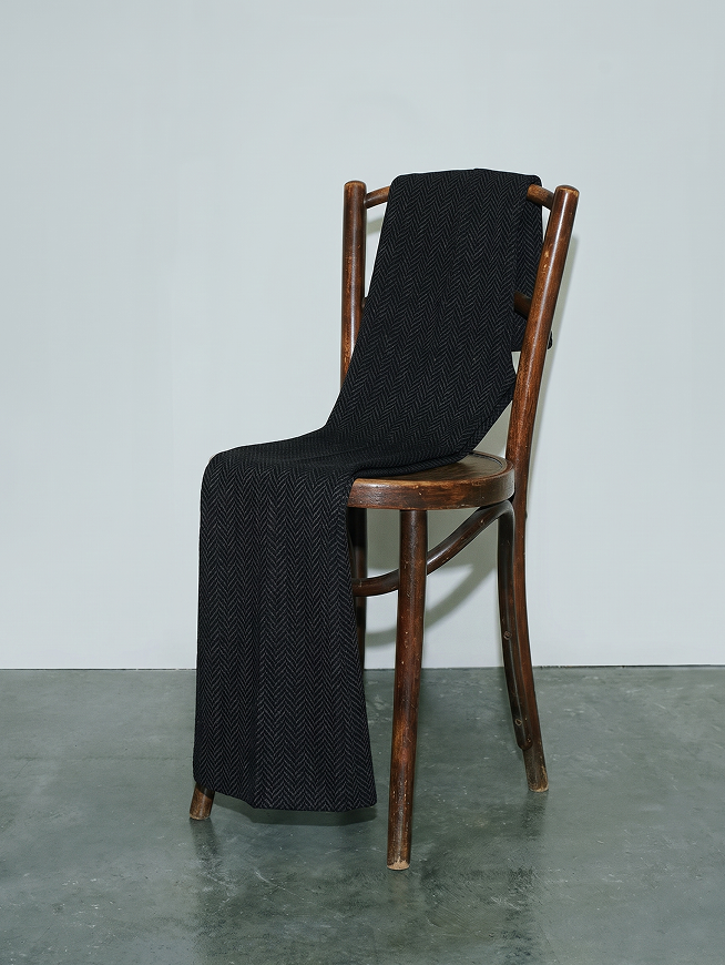 Wooden chair with black herringbone fabric draped over back and seat